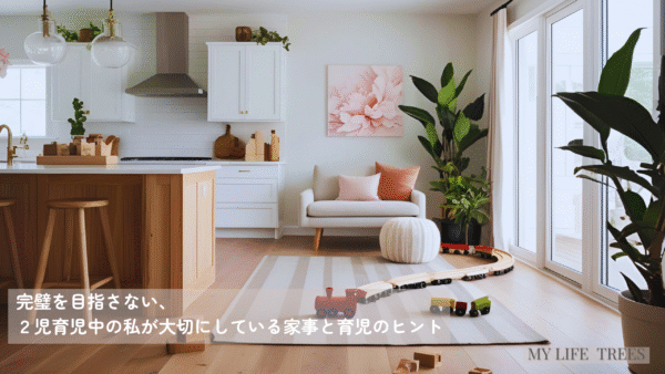 アイランドキッチン越しに見たリビングルーム。グレージュのラグに木製のおもちゃが散らばり、観葉植物とパステルカラーのクッションが並ぶ子育て感のある空間の写真